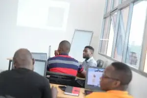 Grupo de ingenieros varones participando en una sesión de capacitación de ProtaStructure en un aula luminosa, usando laptops y prestando atención a una pantalla de proyección.