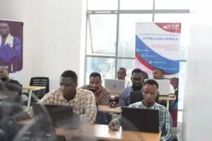 Grupo enfocado de profesionales africanos varones trabajando en laptops en un aula luminosa con pancartas educativas, incluida una que promueve la actualización tecnológica