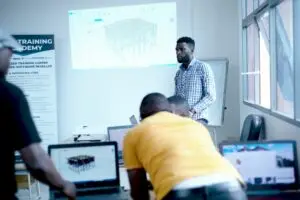Instructor de ingeniería estructural dirigiendo una sesión de capacitación del software ProtaStructure, mostrando un modelo estructural 3D en una pantalla de proyección en un aula.
