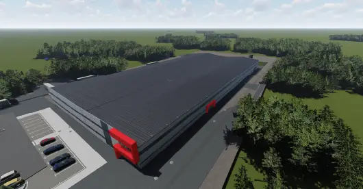 Gran nave industrial moderna de exterior gris y rojo, rodeada de un paisaje verde y árboles densos bajo un cielo parcialmente nublado.