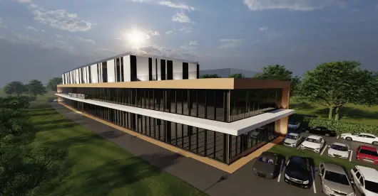 Edificio comercial moderno de dos plantas con grandes ventanales y paneles exteriores de madera y color blanco iluminados, rodeado de césped y una zona de aparcamiento, al atardecer.